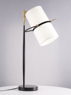 Three-quarter view of this Clérachic table lamp, shade angled sharply right, on a black stem and black marble base with a cord on a white table.