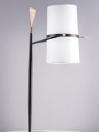 Clérachic table lamp with the shade held upright on a black stem with a gold tip, against a soft lilac-grey backdrop.