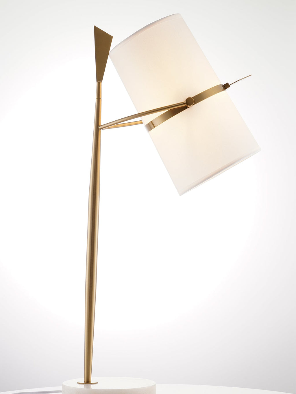 Gold-stemmed Clérachic lamp glowing against a bright white studio backdrop, its cream shade tilted down to the right.
