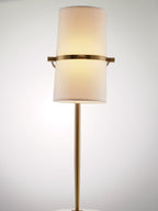 Straight-on view of a Clérachic table lamp lit with warm light, the shade held upright on a gold band and slim gold stem.