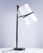 Black Clérachic table lamp on a white table with the shade tilted to the right, against a soft blue-grey backdrop and a trailing cord.