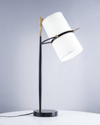 Clérachic table lamp with a black marble base and white shade tilted right, a gold tip at the top, in front of a pale blue-grey wall.