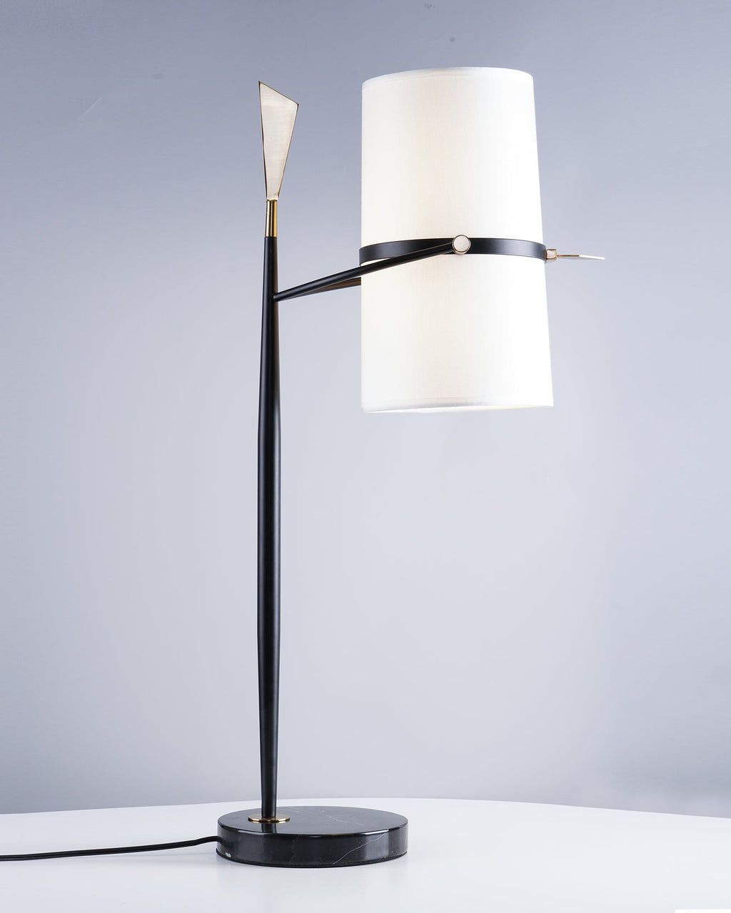 Clérachic lamp with the shade raised level beside the stem, a black marble base and a black cord on a white table.