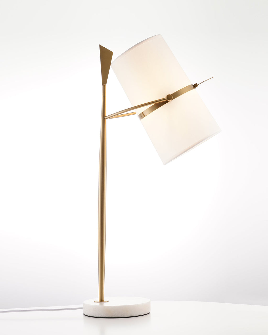 Gold Clérachic table lamp on a white marble base, its softly glowing shade tipped to the right in a bright white studio.