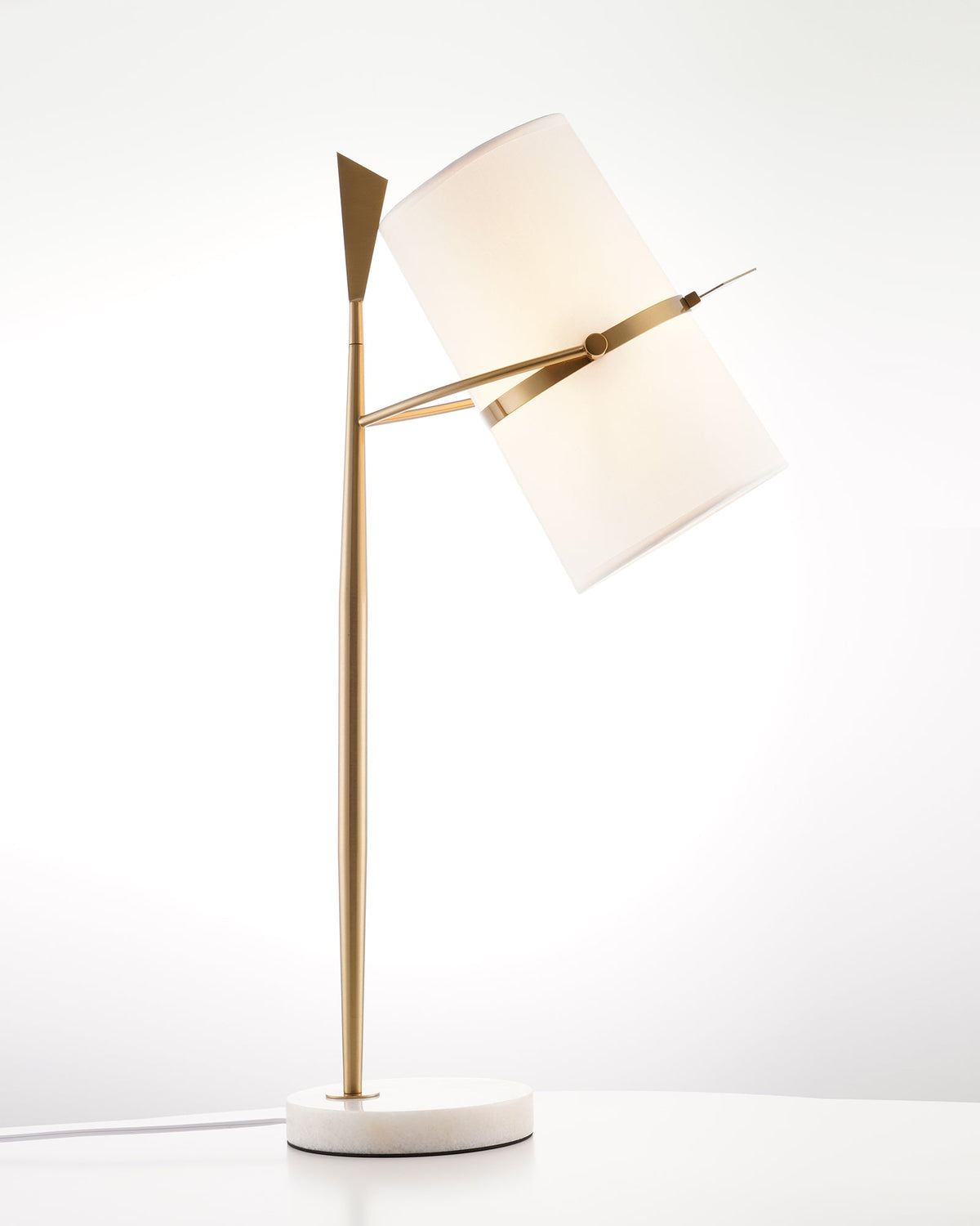 Another view of this gold Clérachic lamp, its glowing white shade tipped right on a round white marble base.