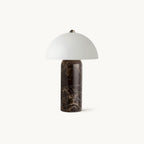 This Clérachic table lamp on a plain white backdrop, with a domed white glass shade above a dark brown veined marble base.
