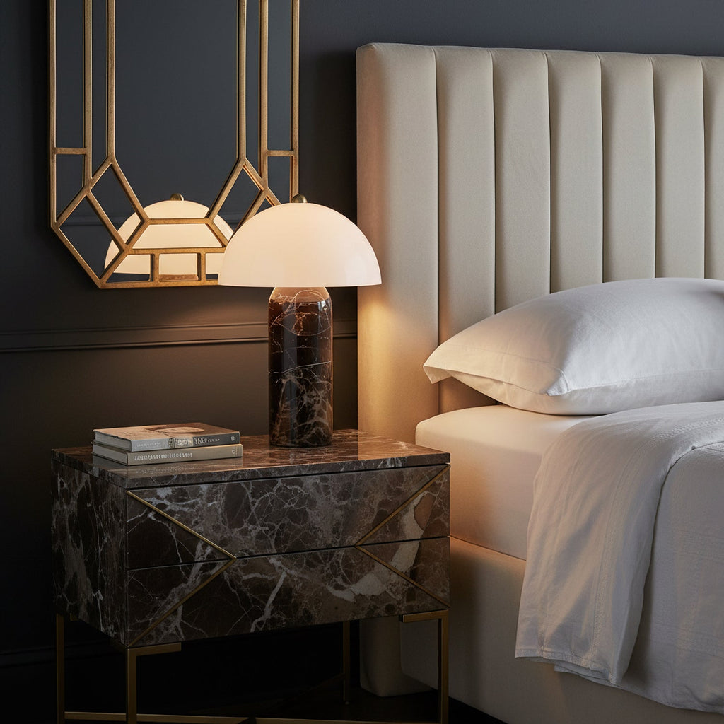 Lit at a bedside, this Clérachic table lamp sits on a marble-fronted nightstand next to an upholstered headboard and white pillows.