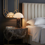 Lit at a bedside, this Clérachic table lamp sits on a marble-fronted nightstand next to an upholstered headboard and white pillows.