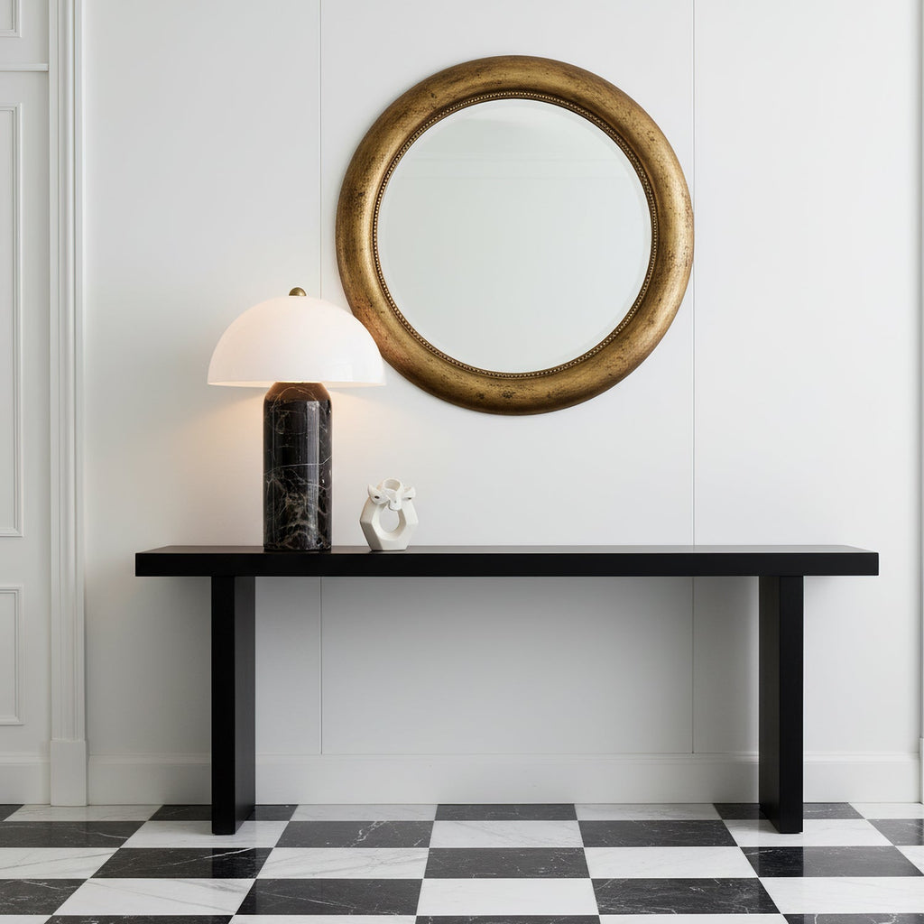 On a black console table in front of a round gilt mirror, this Clérachic table lamp stands over a black-and-white chequered floor.