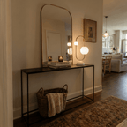 Clérachic table lamp glowing on a console table beneath a mirror in a hallway with a woven basket below.