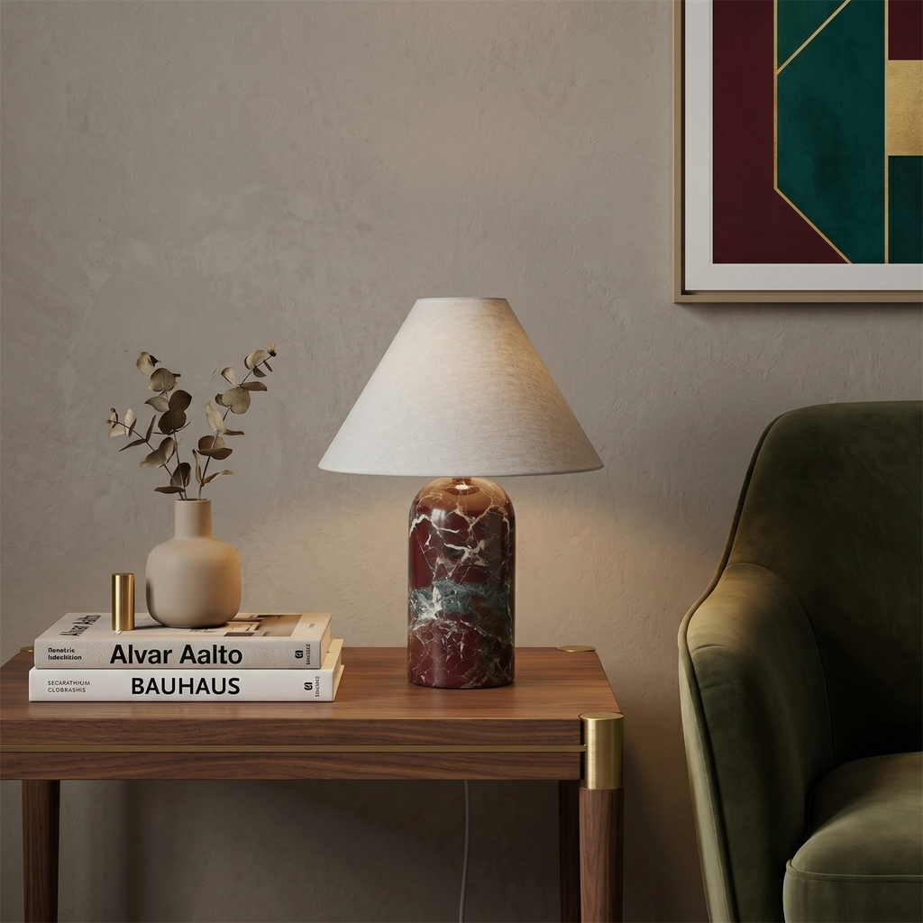 A Clérachic table lamp with a burgundy-veined marble base on a walnut side table, beside stacked art books and a small vase of eucalyptus.