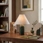 Lit green marble table lamp from Clérachic on a walnut desk, with a bookshelf, a brass globe and a small bud vase nearby.