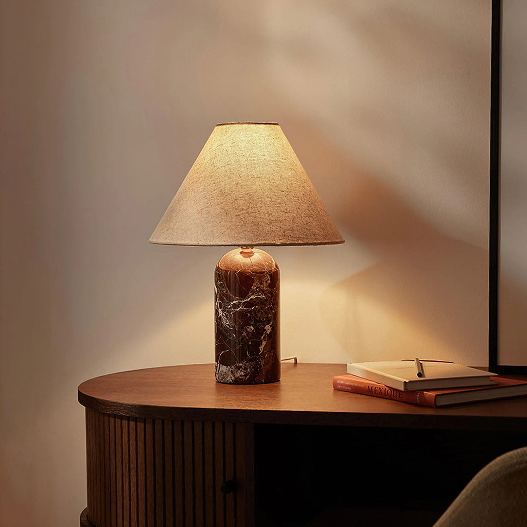 Warm light from a Clérachic table lamp with a dark burgundy marble base, on a curved walnut console with a notebook beside it.