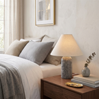 Clérachic table lamp with a grey marble base on a bedside table, next to a neatly made bed with grey and cream cushions.
