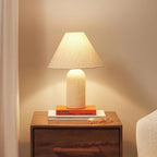 Cream marble base and a glowing linen cone shade on this Clérachic lamp, standing on a stack of books on a bedside chest.