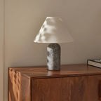 Grey marble base and a white linen shade on this Clérachic table lamp, with dappled sunlight across a walnut chest of drawers.