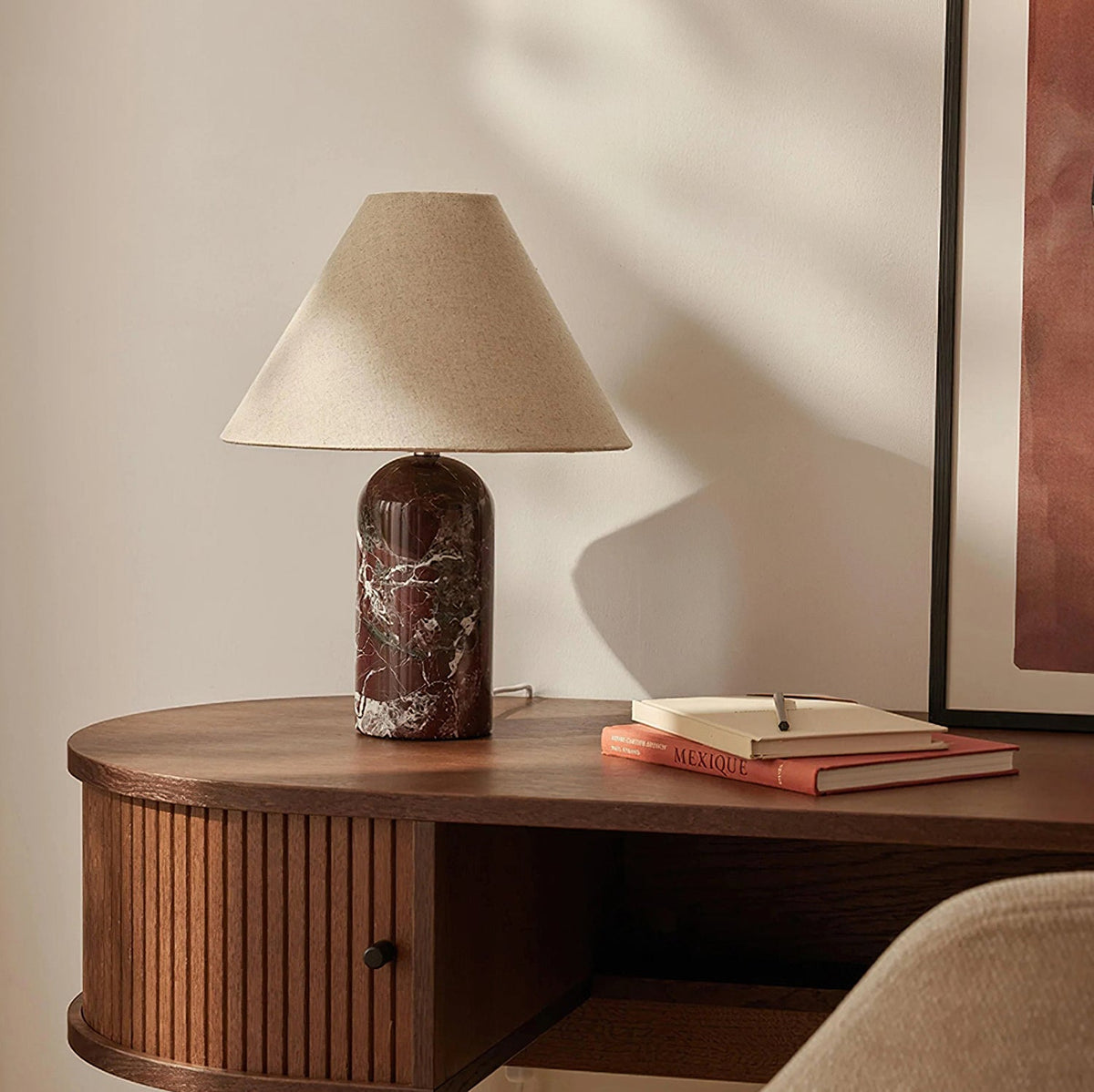 Burgundy marble base on this Clérachic table lamp, with a tan linen shade, on a ribbed walnut console beside a framed print.