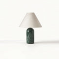Smaller view of this Clérachic table lamp in green marble with a pale linen shade, its white cord trailing on a white backdrop.