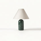 Smaller view of this Clérachic table lamp in green marble with a pale linen shade, its white cord trailing on a white backdrop.