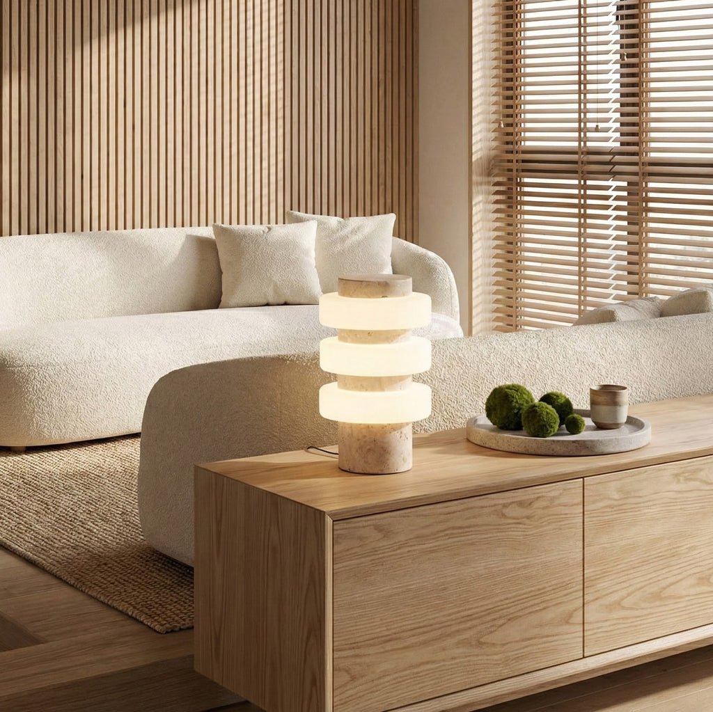 A Clérachic stacked-disc table lamp glows on a pale oak sideboard in a living room with a curved cream sofa and slatted wood walls.