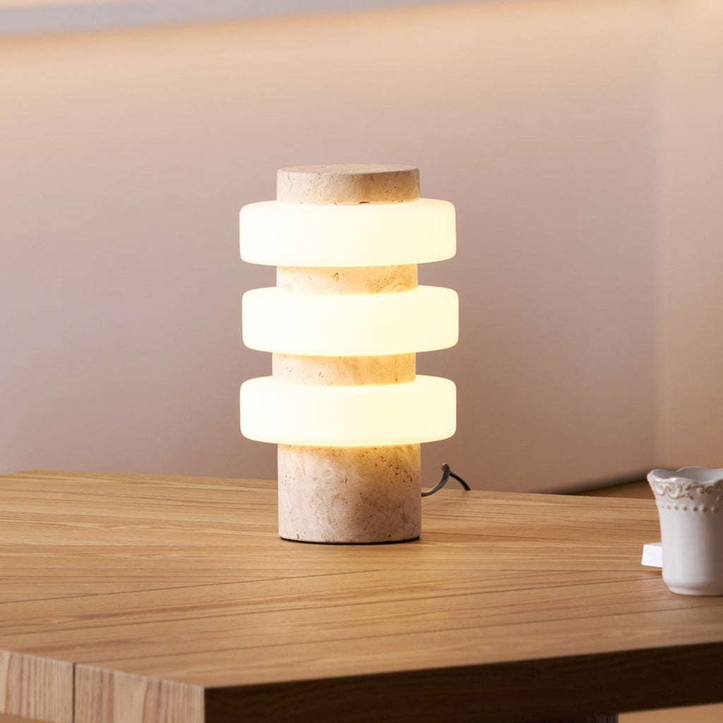 Close view of the lit Clérachic table lamp on an oak table, its three frosted glass discs glowing warm above a beige stone base.