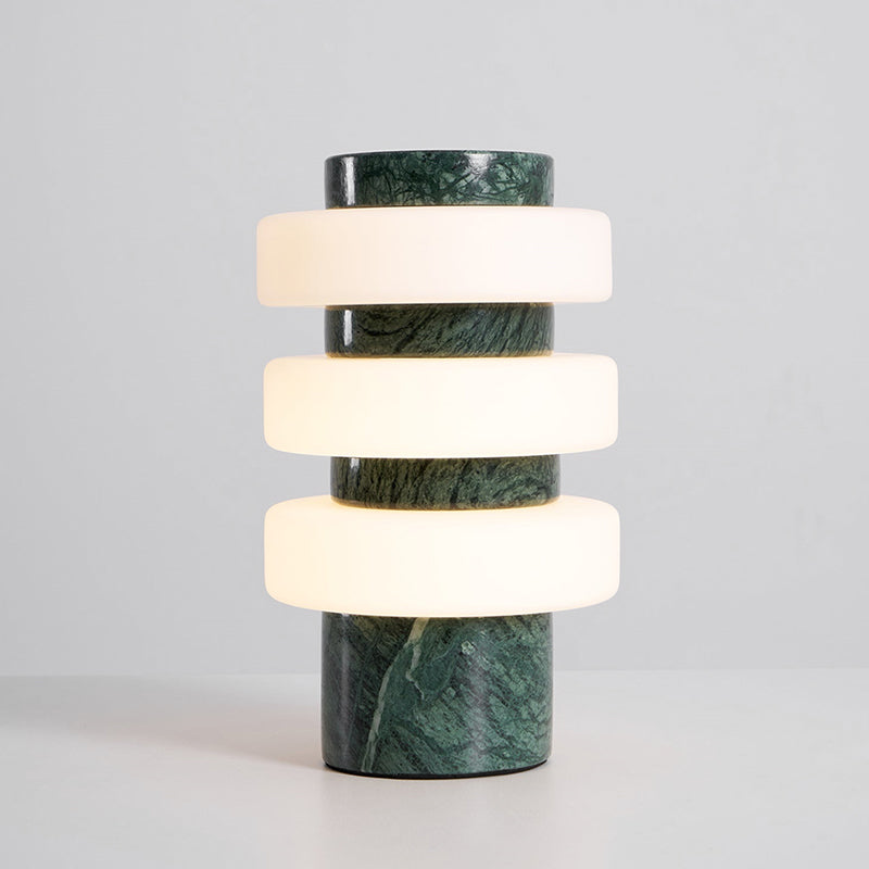 Front view of the lit Clérachic table lamp in the green and white finish, with veined green marble between the glowing glass discs.