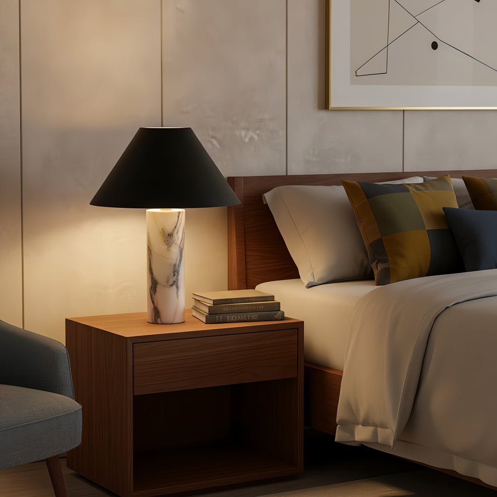 Lit Clérachic marble table lamp on a walnut bedside cabinet, glowing beside a bed with mustard and navy cushions.