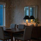 A Clérachic marble table lamp glowing on a dining-room sideboard, its twin reflected in the mirror above, with a dark wood table in front.