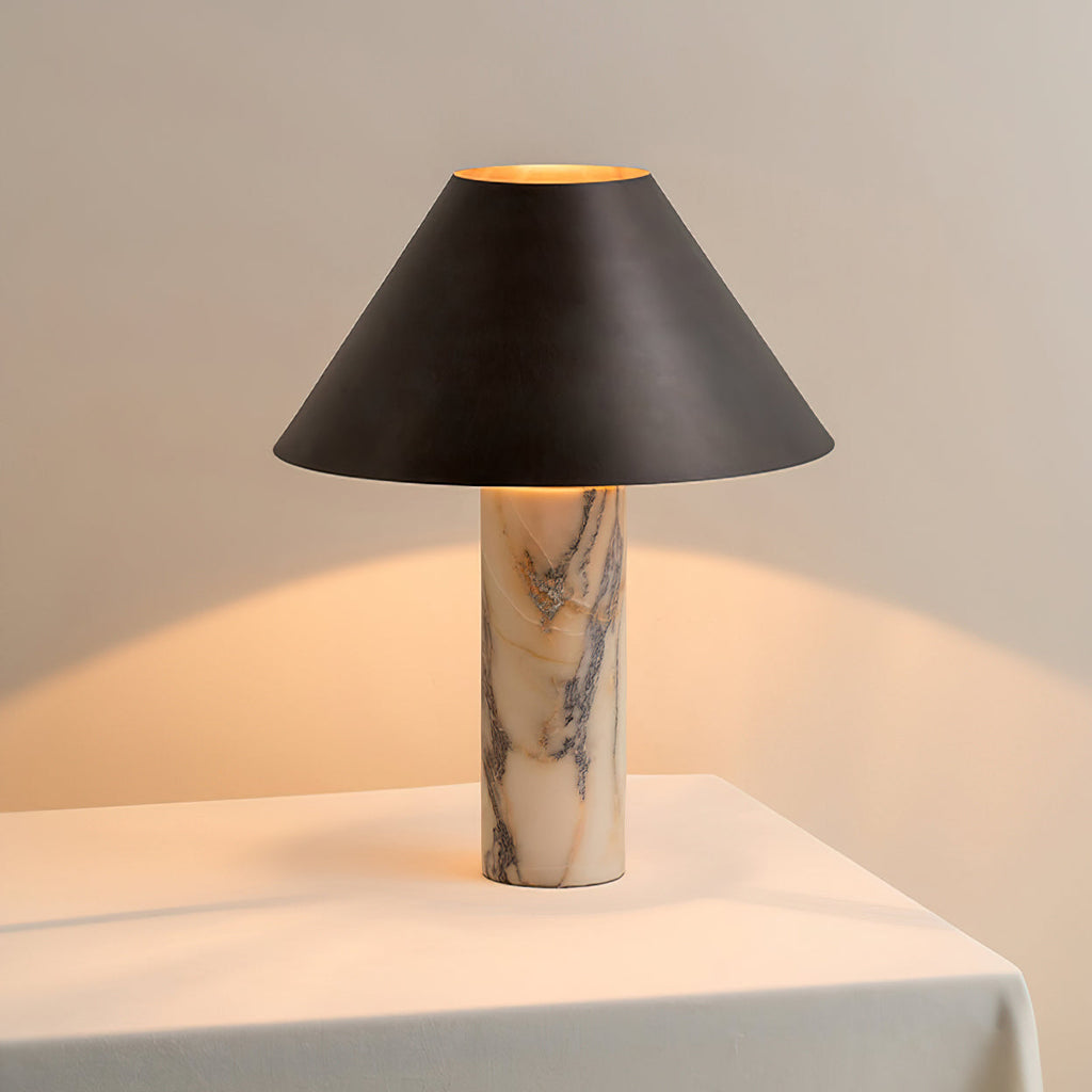 Warm light spills from under the black shade of this Clérachic marble lamp, standing on a white-draped table against a pale wall.