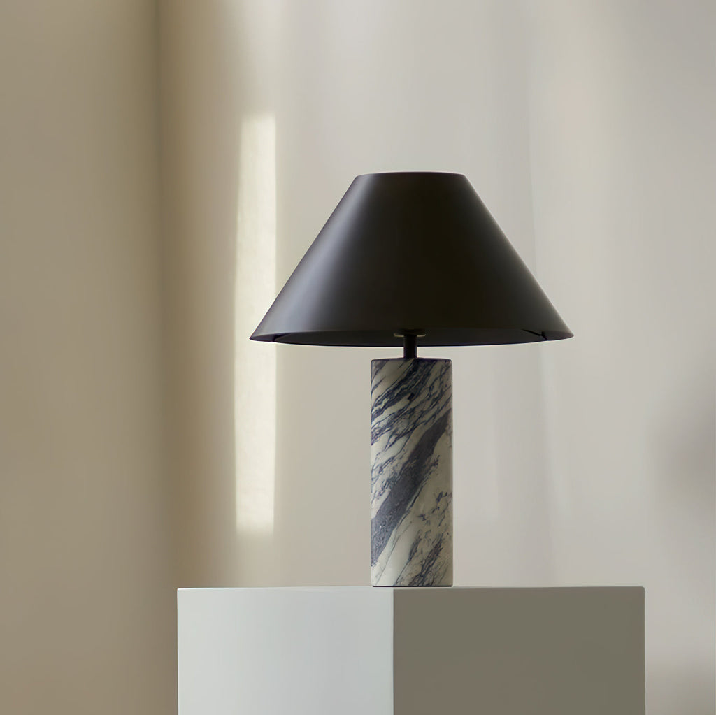 Small Clérachic table lamp with a marble column base, standing on a white block against a soft cream wall.