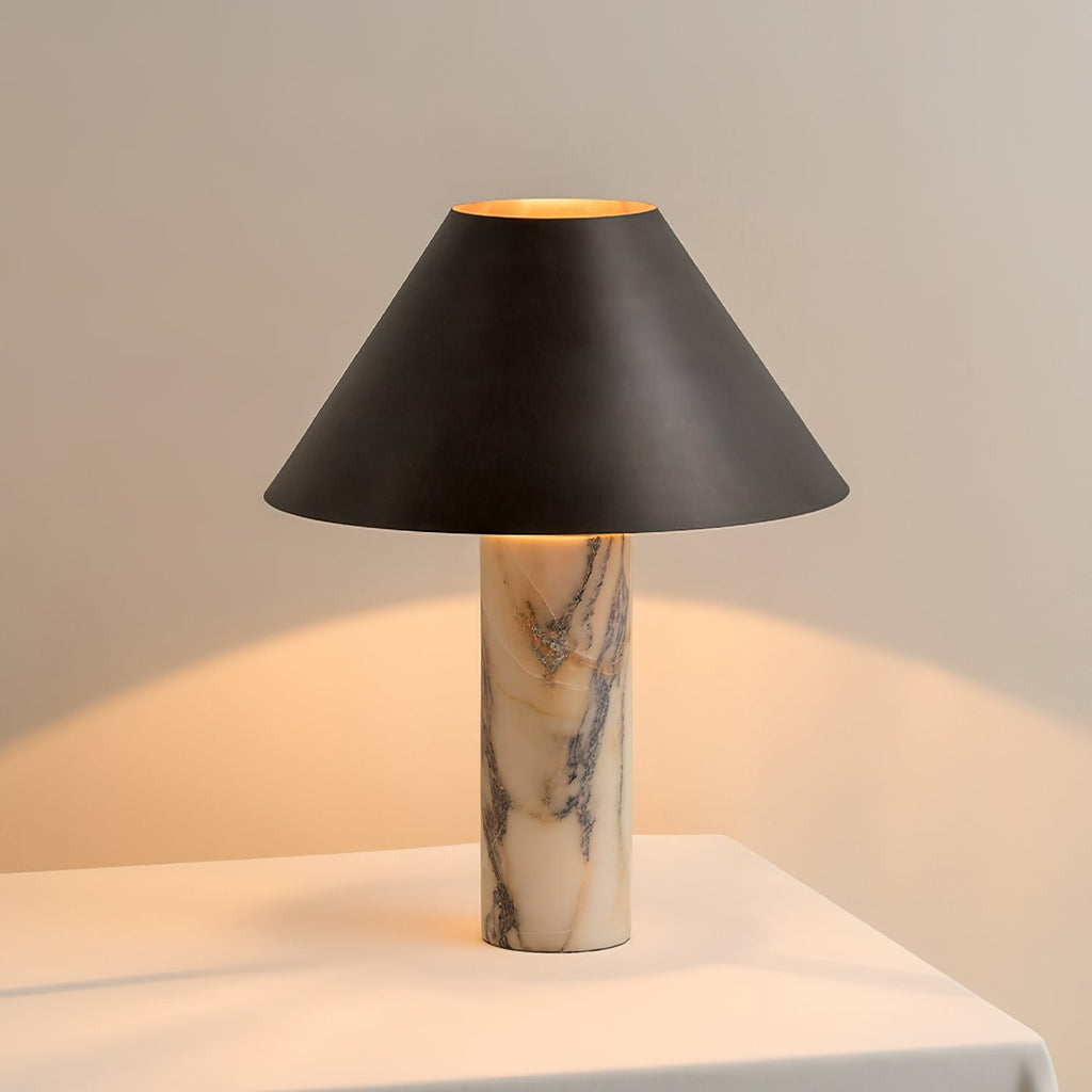 Lit Clérachic table lamp on a white table, the inside of its black shade glowing gold and warming the wall behind.