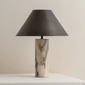 Straight-on view of this Clérachic table lamp, unlit, with its black conical shade above a cream marble base on a white table.