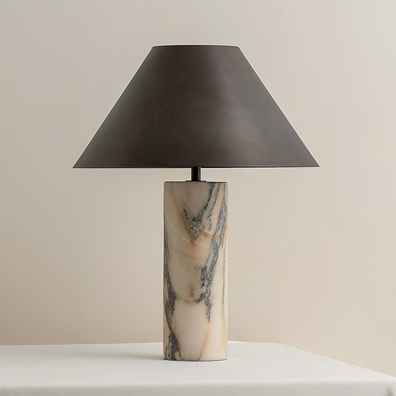 Straight-on view of this Clérachic table lamp, unlit, with its black conical shade above a cream marble base on a white table.