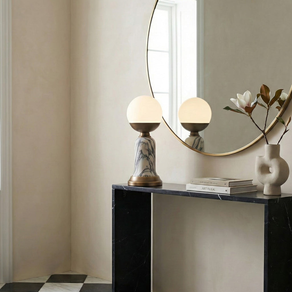 A Clérachic table lamp on a black console beneath a round mirror, with a sculptural white vase and a magazine alongside.