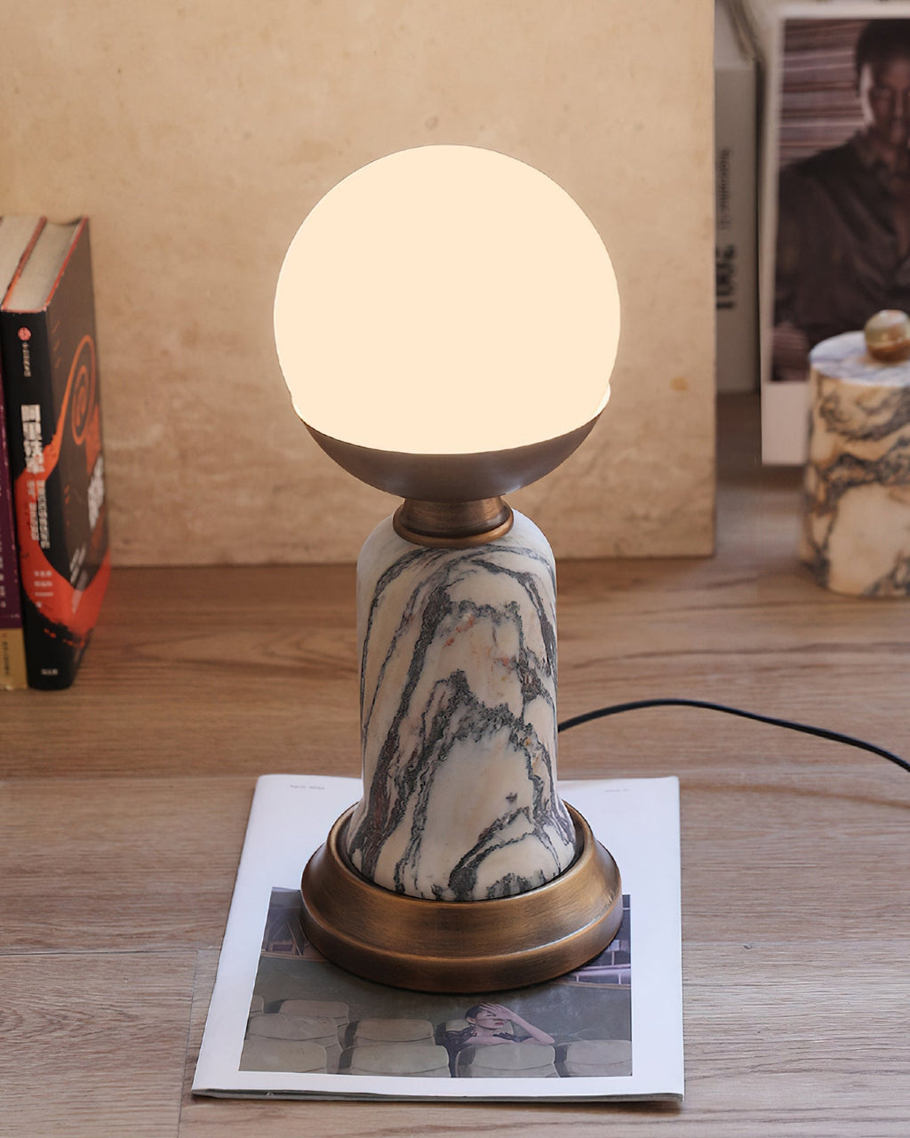 Pictured here, a lit Clérachic table lamp on a wood floor, with its black cord trailing to the right and a magazine under its base.
