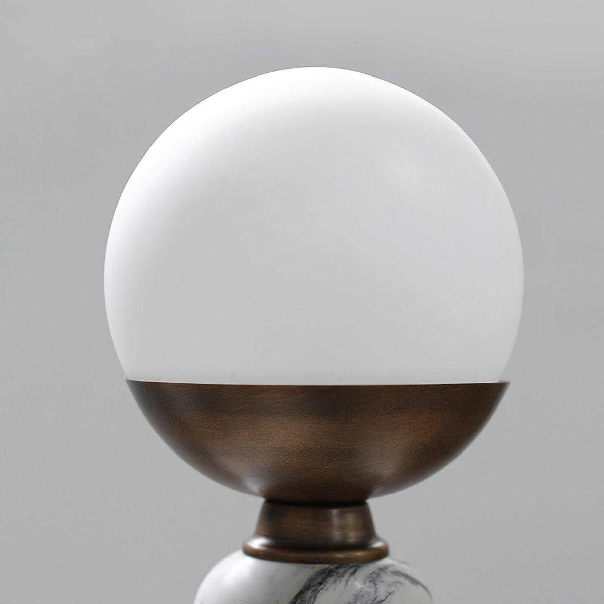 Close view of the opaque white globe and the bronze cup that holds it, on this Clérachic table lamp.