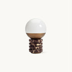 This Clérachic table lamp on a plain white backdrop, a white glass globe above a bronze cap and a ribbed red-and-cream marble base.