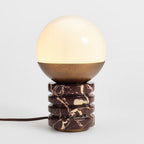 Close view of this Clérachic lamp lit, the opal globe glowing above a bronze cap and a ribbed marble base with cream veining.