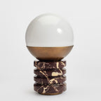 Unlit Clérachic table lamp on a pale grey backdrop, its white globe, bronze collar and stacked marble rings in focus.