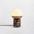 Distant view of this Clérachic table lamp lit on a pale grey backdrop, its brown cord trailing out of the frame at the left.
