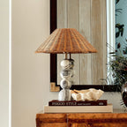 Clérachic table lamp with a stacked marble base and rattan shade on a burr wood cabinet, in front of a dark-framed mirror.