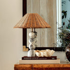 Front view of a Clérachic marble and rattan table lamp in front of a mirror, a sculpted cream bowl at its foot.