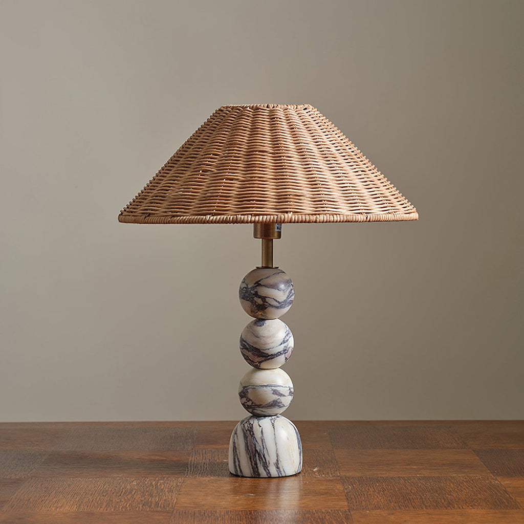 Unlit Clérachic table lamp with grey-veined marble spheres and a woven rattan shade, on a wooden table against a grey wall.