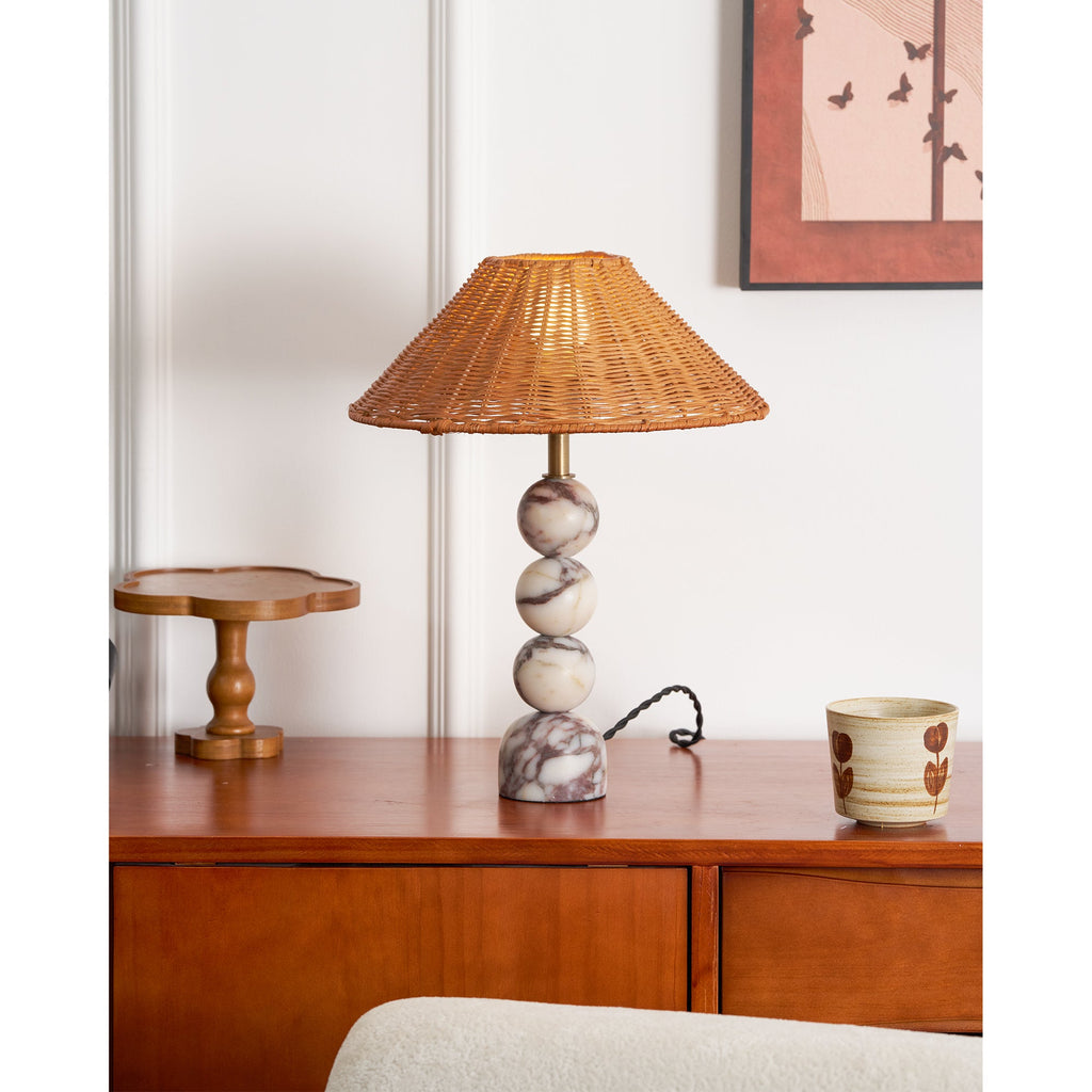 Clérachic rattan table lamp with a veined marble base on a wood sideboard, a twisted black cord and a painted cup beside it.