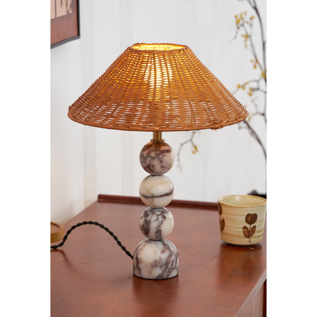 Close view of a lit Clérachic lamp on a teak sideboard, its marble spheres beside a hand-painted cup and a twisted cord.