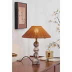 Portrait view of a lit Clérachic rattan lamp on a wooden sideboard, under a framed butterfly print and a blossom branch.