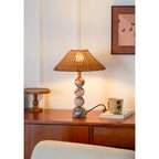 Clérachic marble and rattan lamp glowing on a sideboard, with a small wooden stand to the left and a cream chair in front.