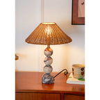 Tight view of this Clérachic lamp's marble spheres and glowing rattan shade, with a black twisted cord on a teak surface.