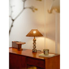 Wide view of a lit Clérachic lamp on a teak sideboard, with a retro radio, a wooden stand and a cup on a book.