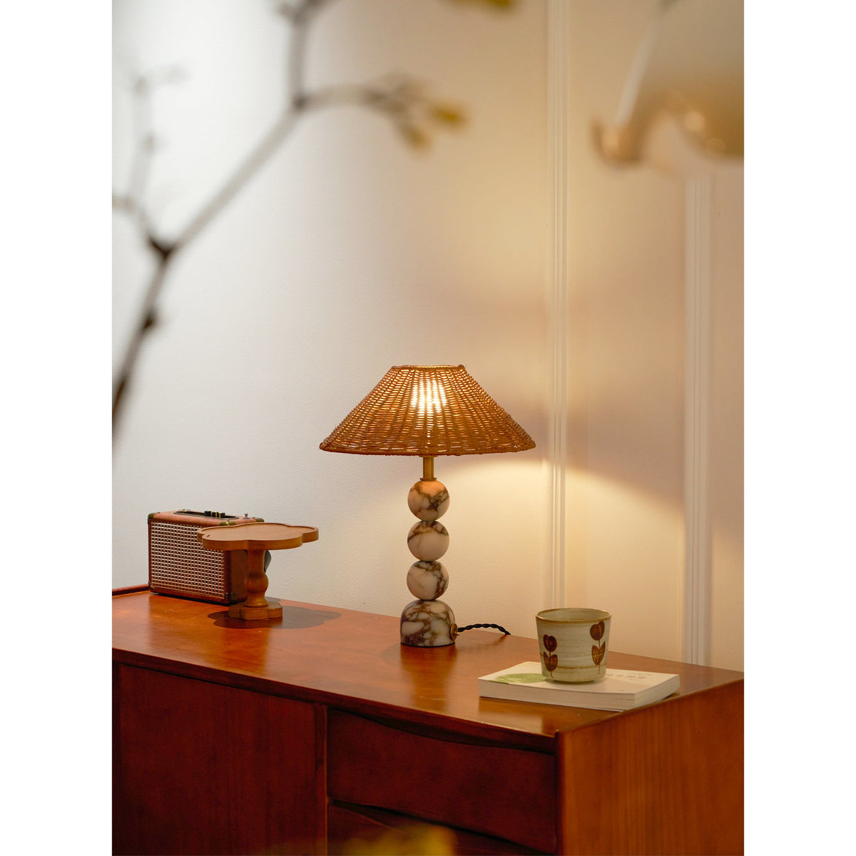 Wide view of a lit Clérachic lamp on a teak sideboard, with a retro radio, a wooden stand and a cup on a book.